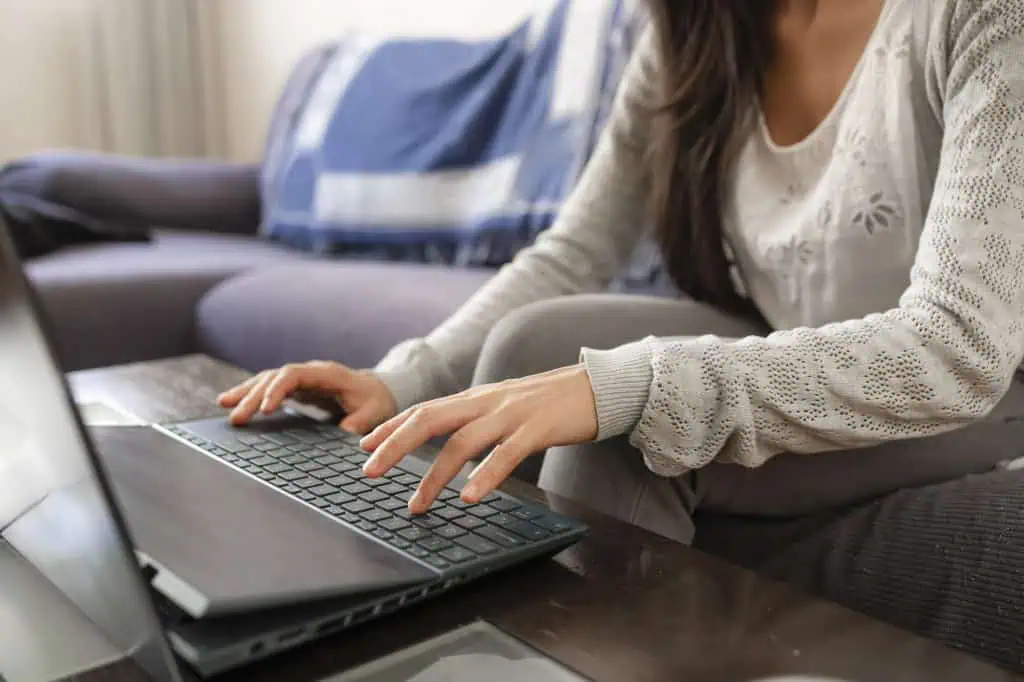 a woman surfs the internet and types on the keyboard of her laptop while sitting on the sofa at home.