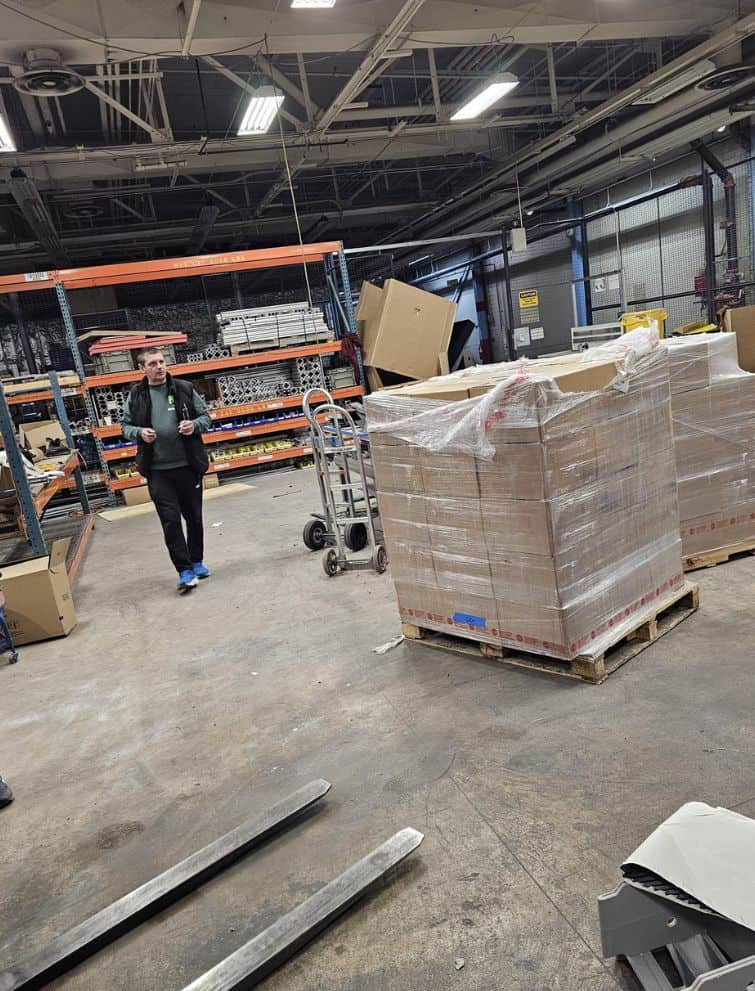 Warehouse worker managing large pallet of boxed items in industrial storage facility.