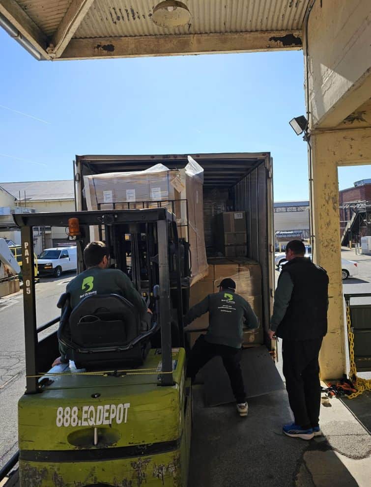 Moving truck unloading with workers at a loading dock.
